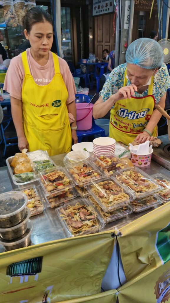 Vendors in yellow aprons behind their food trays
